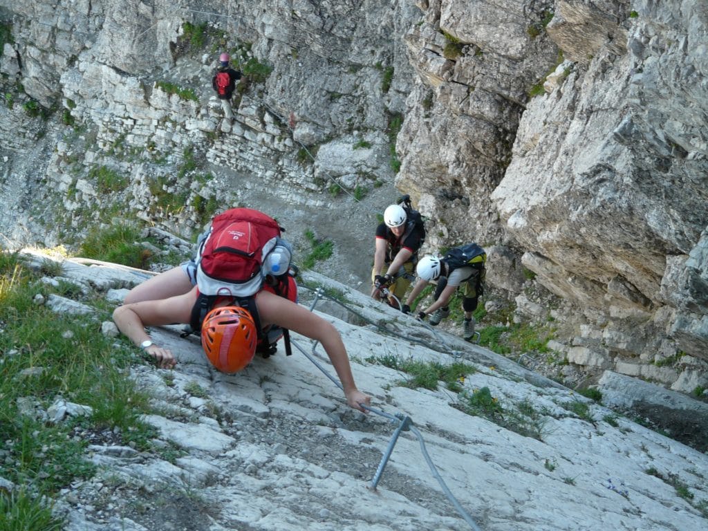 Jugendliche besteigen in Kletterausrüstung gemeinsam einen Berg.